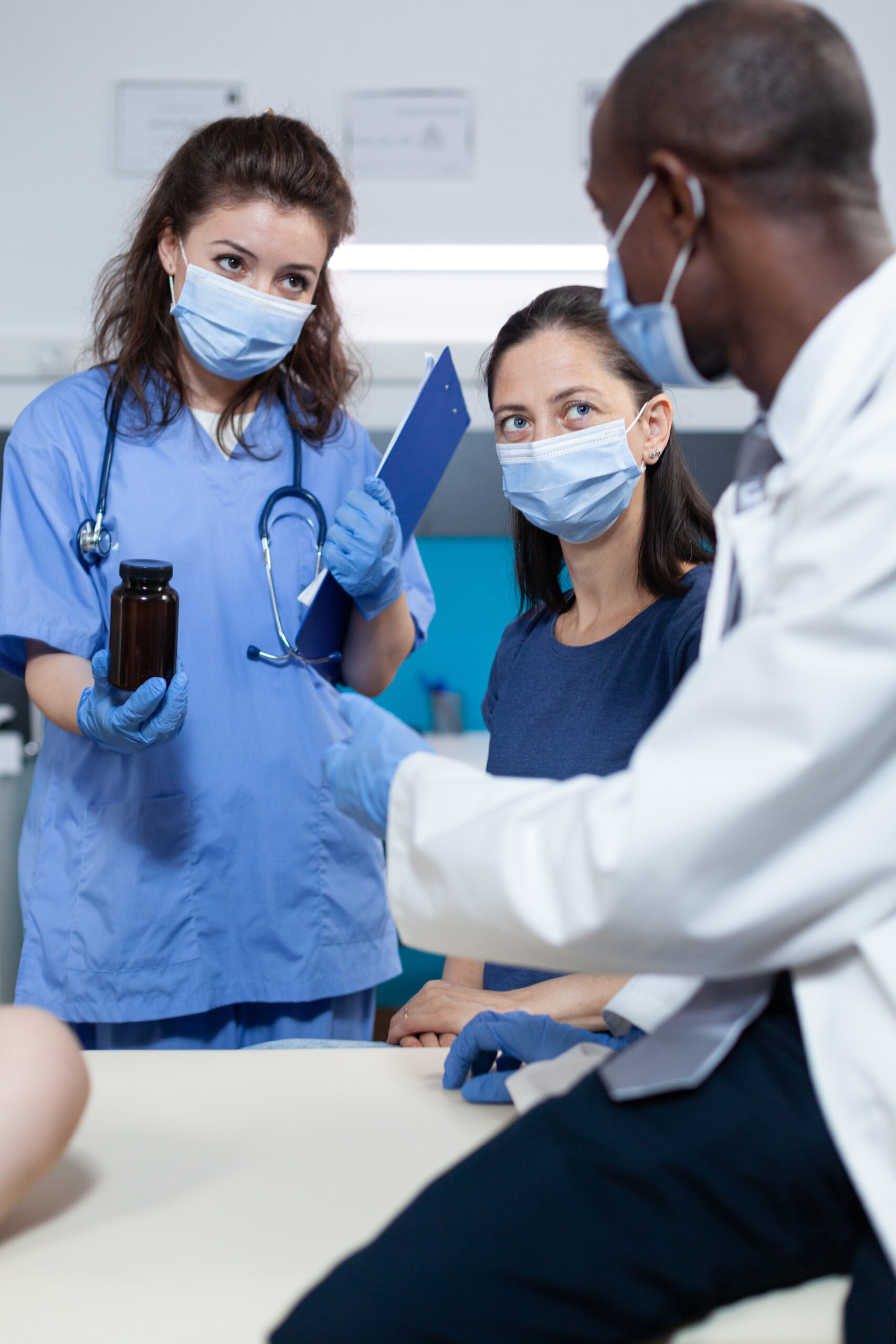 African american pediatrician doctor with protection face mask against coronavirus discussing antibiotics treatment with family during clinical consultation in hospital office. Health care service