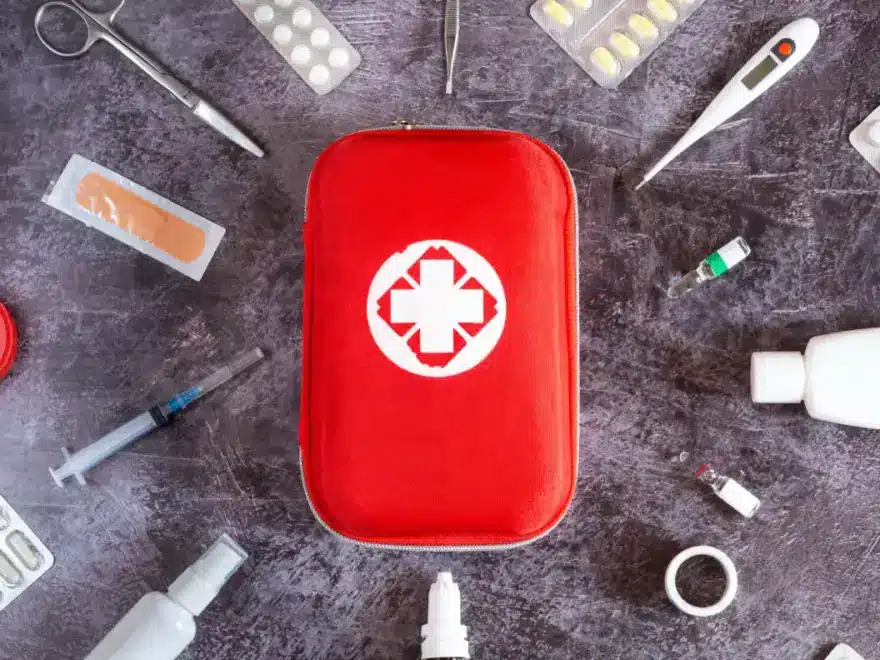 Red home first aid kit surrounded by plasters, a thermometer and bandages